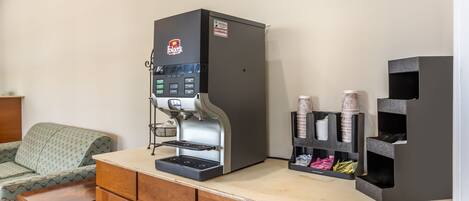 A coffee machine with a control panel, a small table, and a storage unit with cups and napkins.