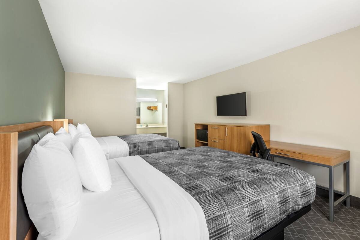 Une chambre d’hôtel avec deux lits, un bureau, une chaise, une télévision et une armoire.