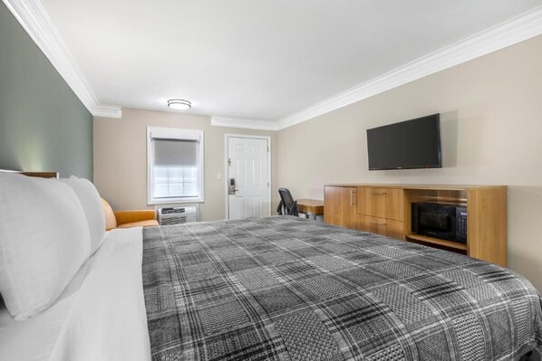 Habitación de hotel con una cama grande, un televisor de pantalla plana montado en la pared, un mueble de madera con microondas y una ventana con persianas.