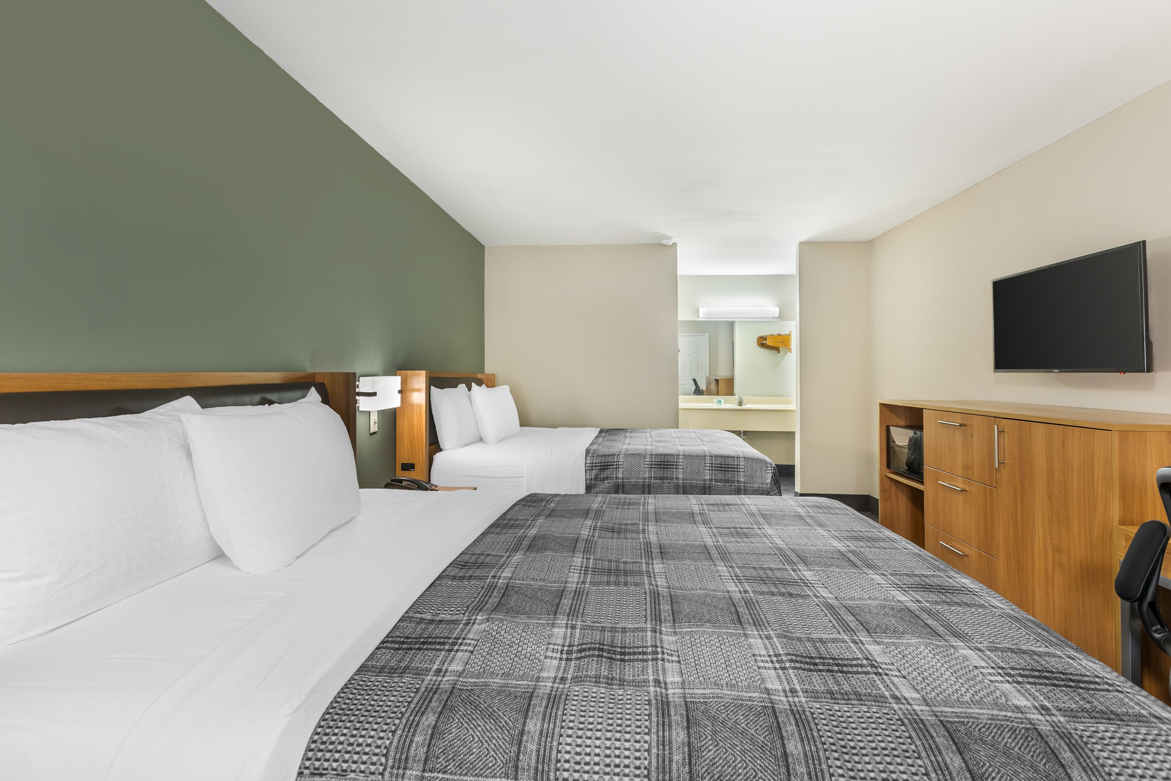 A hotel room with two beds, a television, a wooden cabinet, and a mirror.