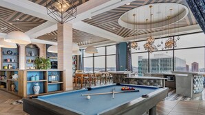Una mesa de billar en una habitación moderna con vistas a la ciudad, estanterías y una zona de bar.