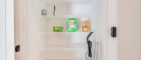 A white interior with a door, a shelf with cleaning supplies, and a power outlet.
