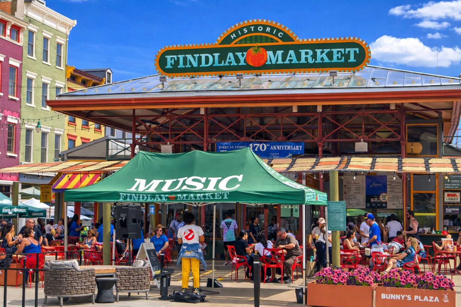 Un mercado histórico con un cartel llamativo de Findlay Market y una carpa verde que anuncia música.