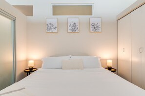Une chambre d’hôtel avec un grand lit, deux tables de chevet avec des lampes et trois œuvres d’art florales encadrées accrochées au mur.