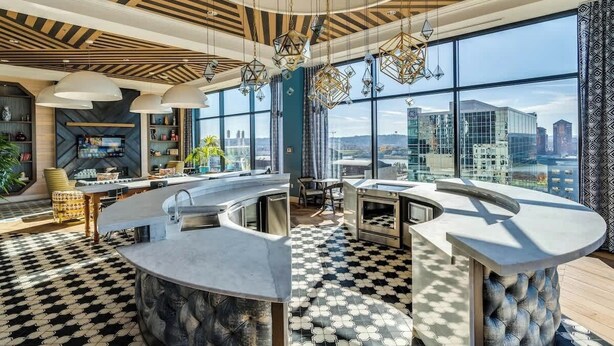 A modern kitchen with a curved island, large windows, and a city view. - Downtown King w/Rooftop Access | Hot Tub (Cincinnati)