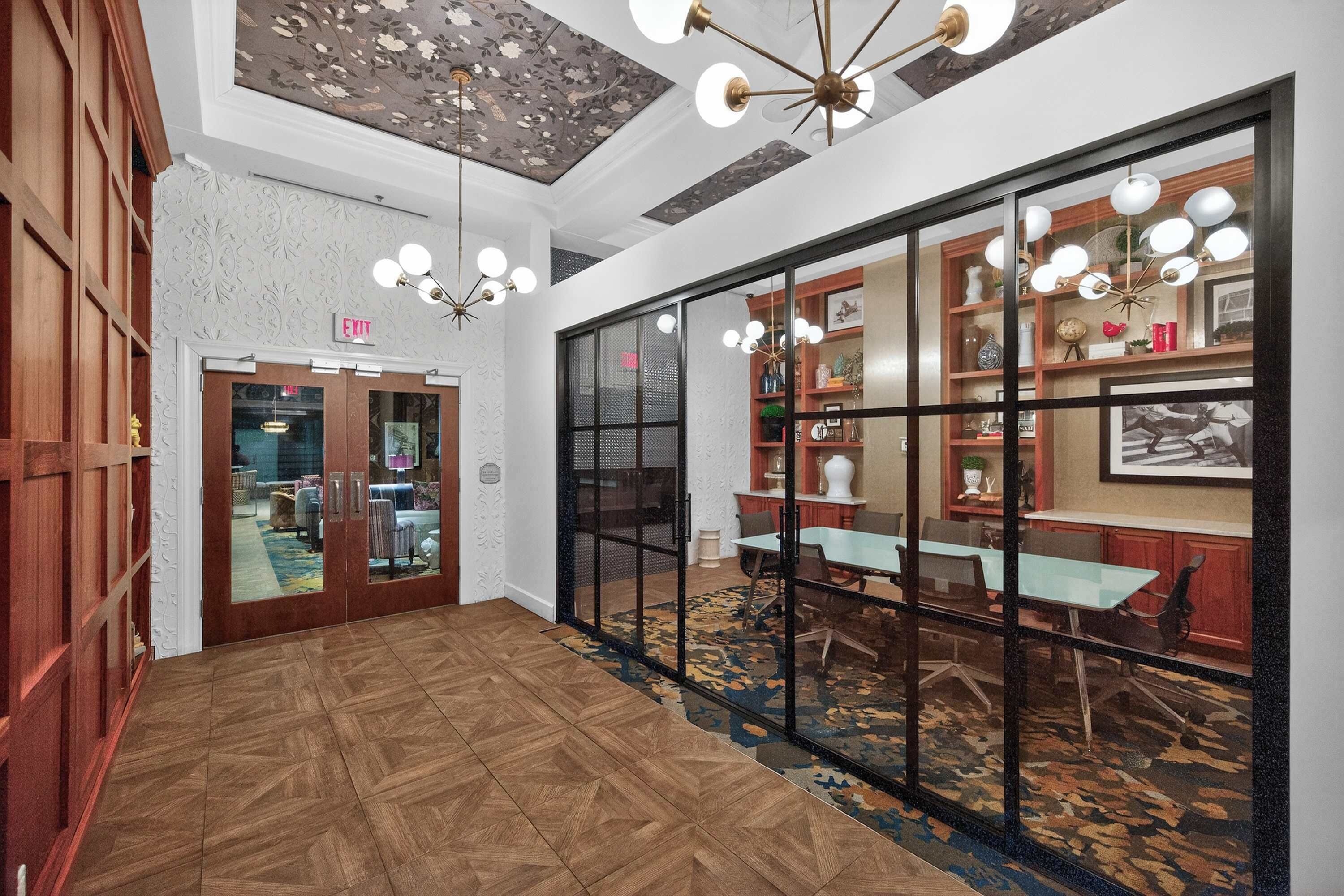 A hotel lobby with a wooden floor, a glass partition, and a ceiling with a floral pattern.