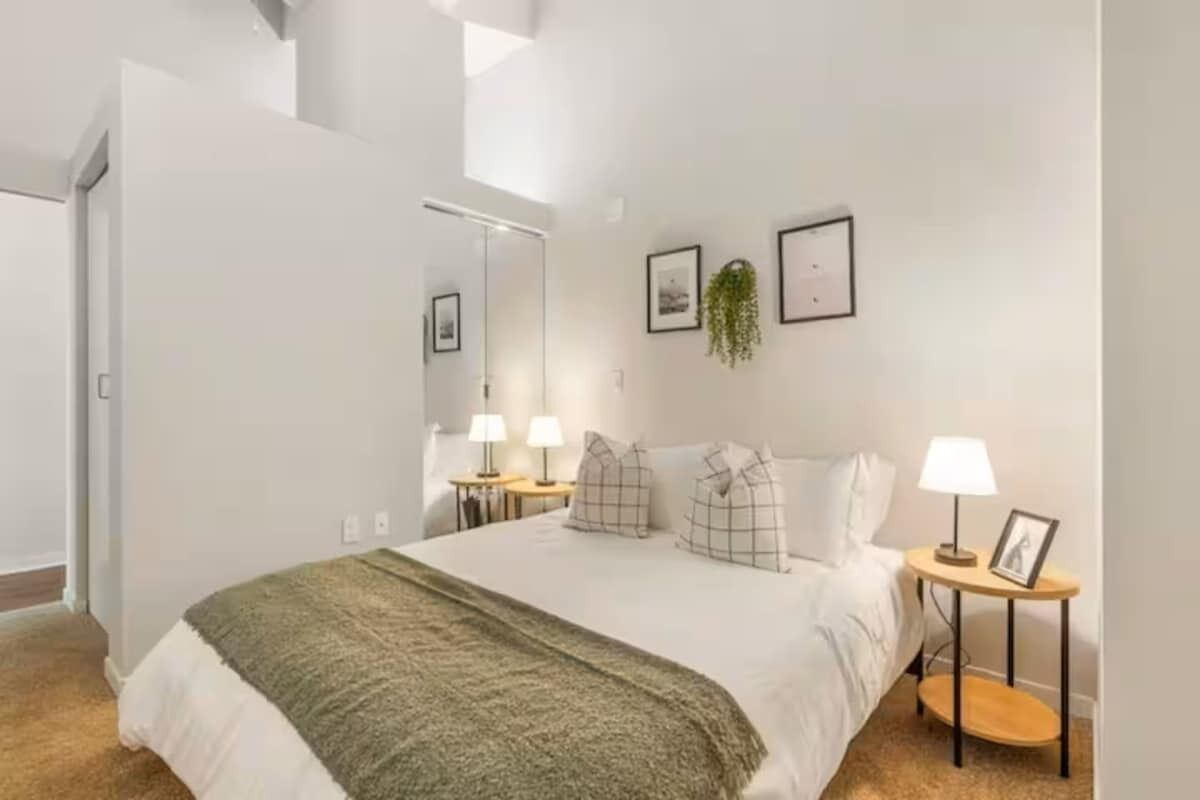 Une chambre à coucher moderne, avec un lit, des tables de chevet, des lampes et des tableaux encadrés accrochés au mur.