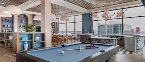 Mesa de billar en una habitación moderna con vistas a la ciudad, estanterías y una zona de bar.