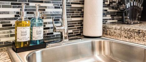 A kitchen sink with a modern faucet, two bottles of dish soap, and a paper towel holder.