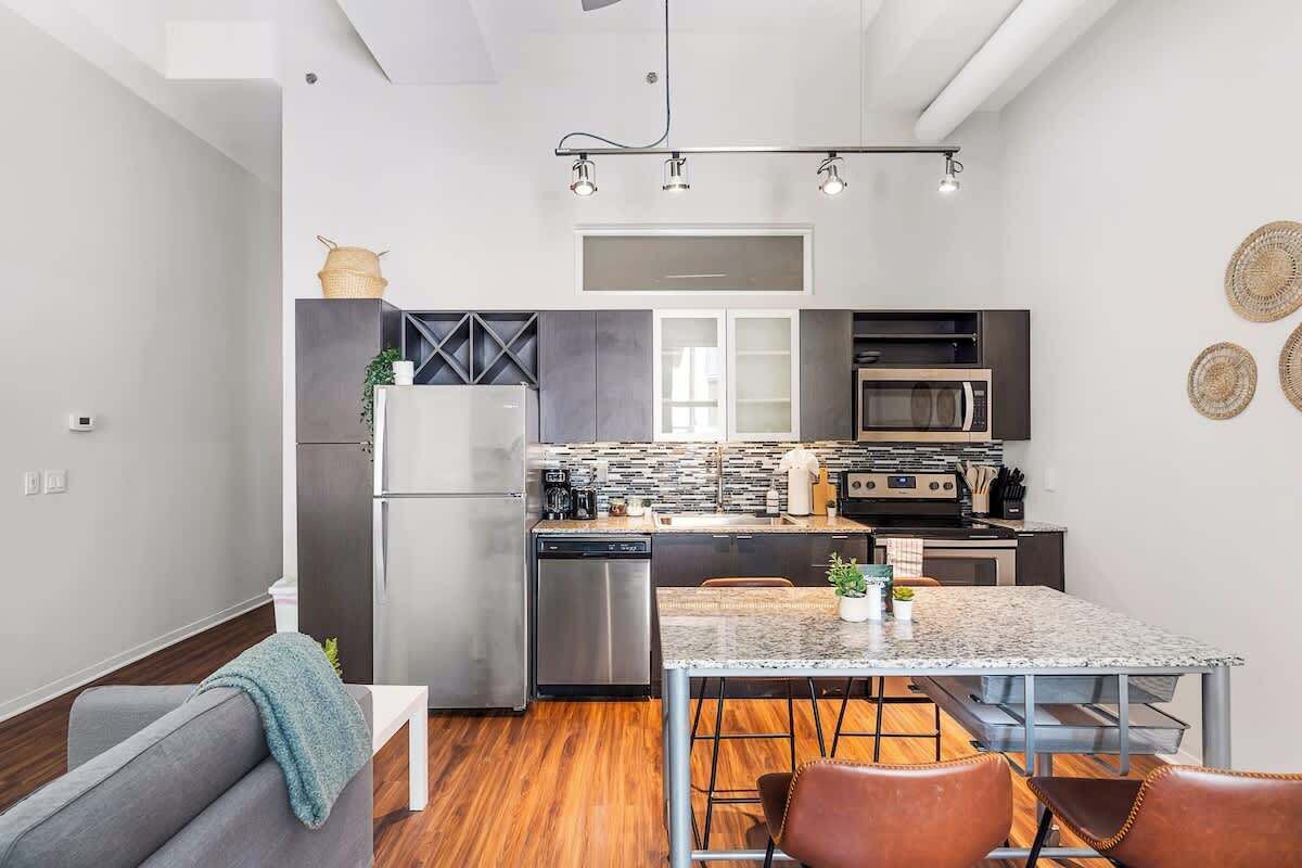 Een moderne keuken met roestvrijstalen apparatuur, een eetgedeelte met een marmeren tafel en een gezellige zithoek met een bank en stoelen.