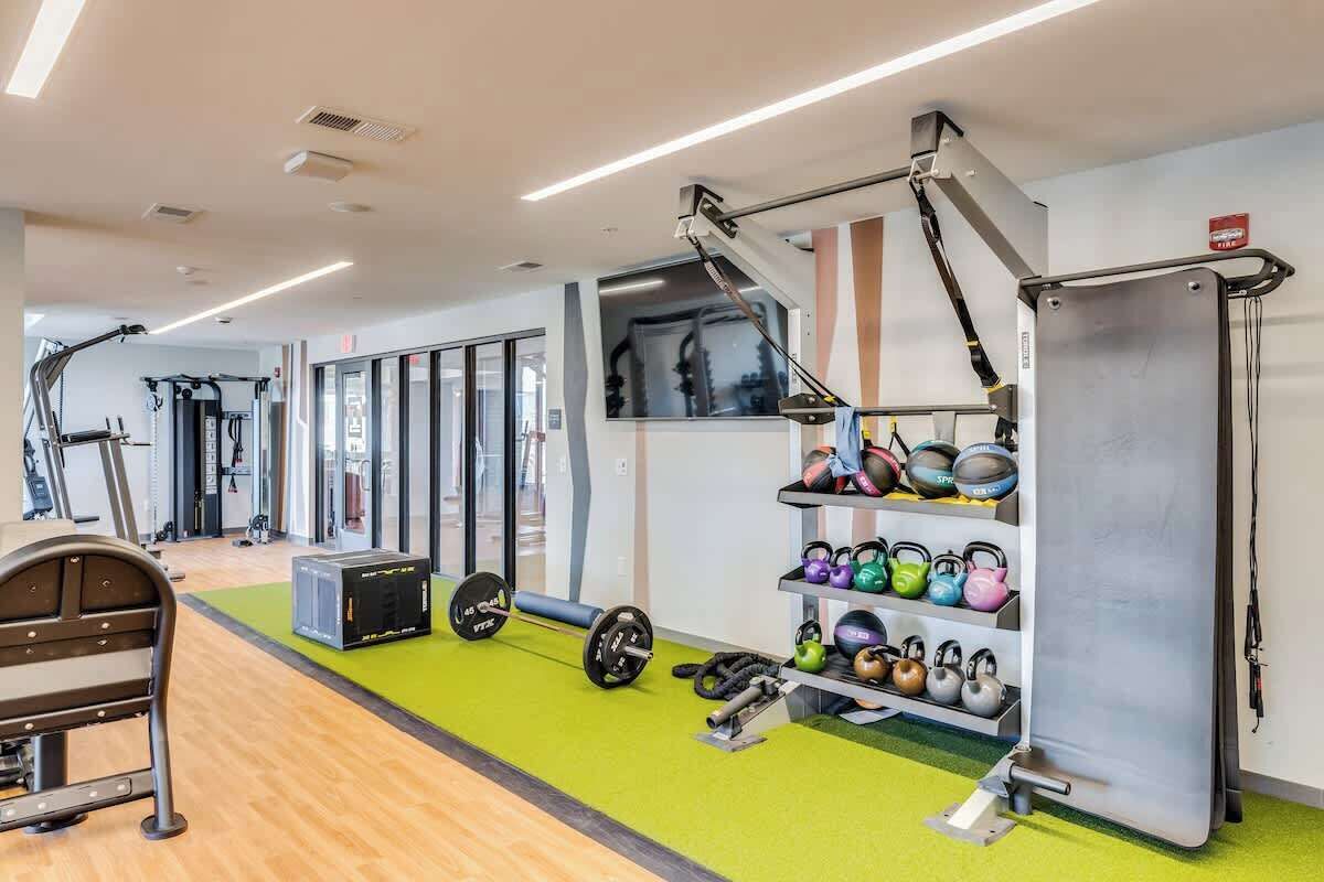 Een sportschool met fitnessapparatuur, een bank, een rack voor gewichten en een wandplank met kettlebells.