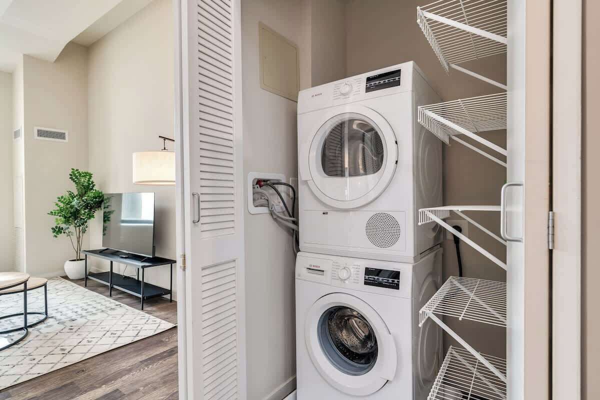A laundry room with stacked washers and dryers, a potted plant, and a TV.