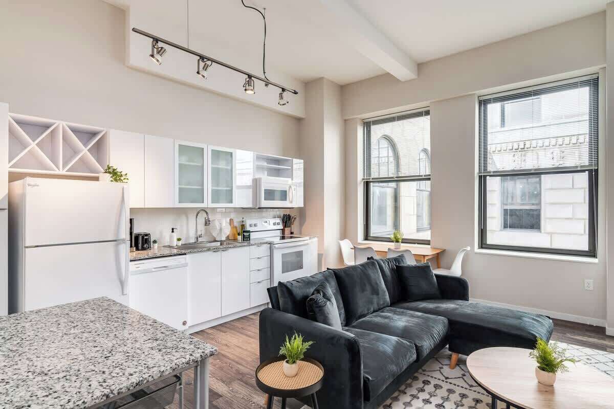 A modern kitchen with white cabinets, a black leather sofa, and a dining area with a table and chairs.