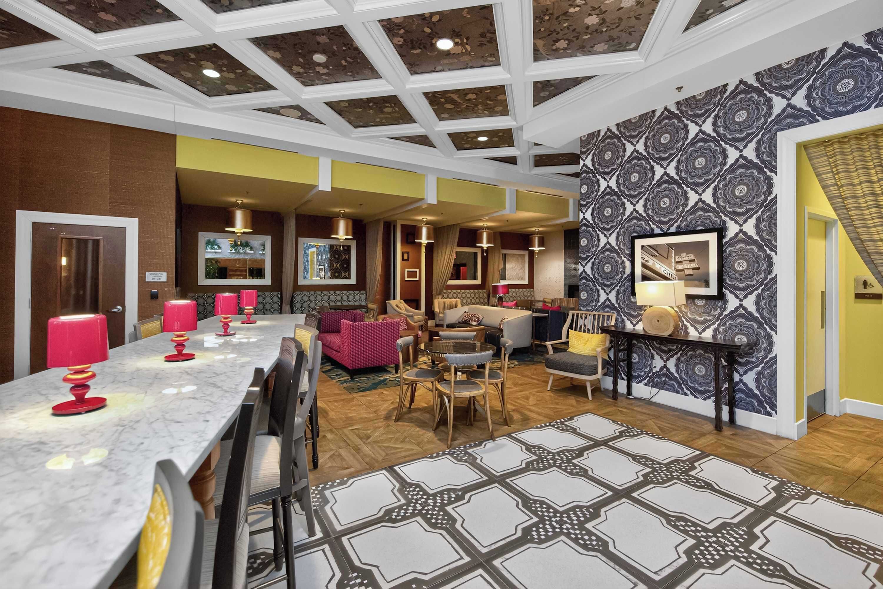 A spacious hotel lobby with a marble reception desk, plush seating, patterned wallpaper, and a high ceiling with decorative beams.