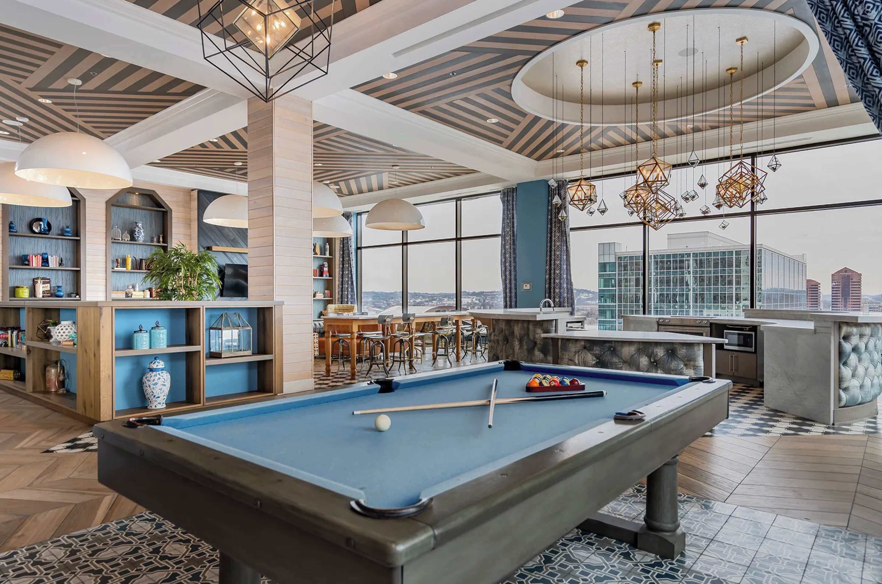 Una mesa de billar con accesorios para jugar, una zona de bar y un espacio de estar con vista a la ciudad.