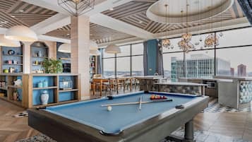 Una mesa de billar con accesorios para jugar, una zona de bar y un espacio de estar con vista a la ciudad.