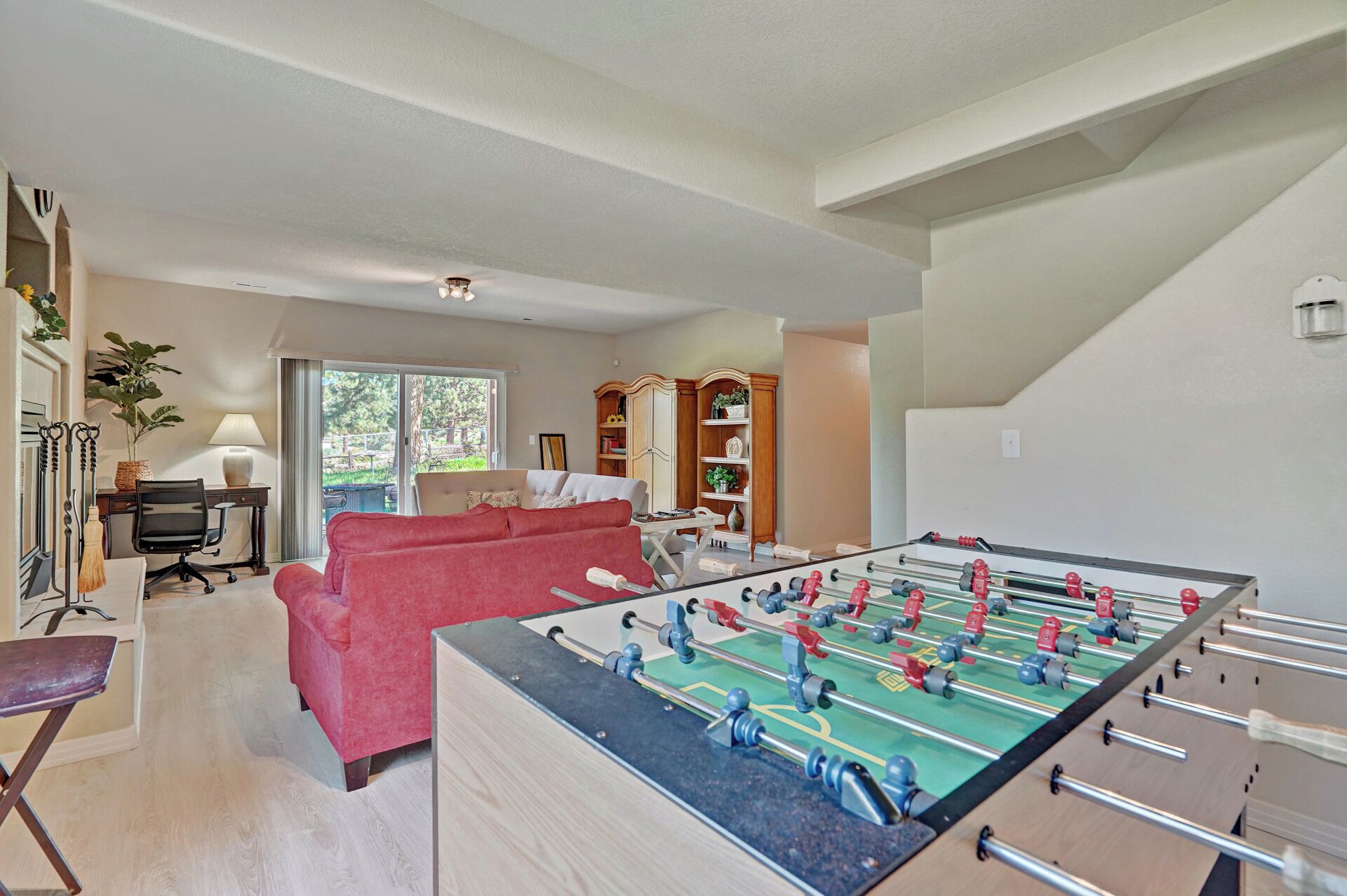 A spacious living room with a foosball table, a red sofa, and a desk with a lamp.