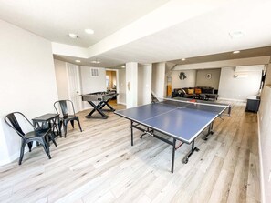 Una habitación amplia con mesa de ping pong, sillas y una pequeña mesa con mesa de futbolín.