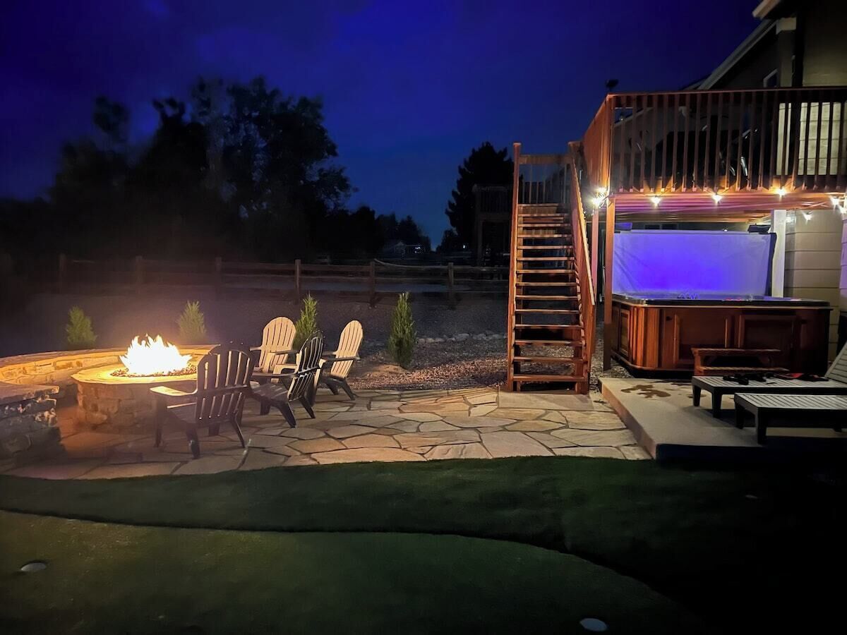 A patio area with a fire pit, Adirondack chairs, and a hot tub.