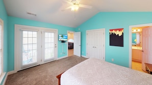 A bedroom with a bed, two doors, a ceiling fan, and a TV in the background. - Caribbean Cove 504 (Myrtle Beach)
