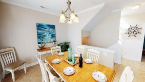 A dining area with a wooden table set for four, white chairs, a chandelier, a painting, and a ship's wheel decoration. - Caribbean Cove 504 (Myrtle Beach)