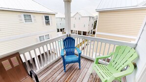 A wooden deck with a blue and green Adirondack chair, white railings, and a view of neighboring houses. - Caribbean Cove 504 (Myrtle Beach)