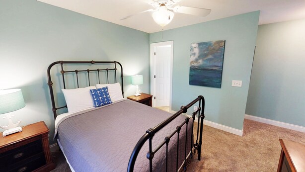 A bedroom with a bed, nightstands, a ceiling fan, a painting, and a door. - Caribbean Cove 504 (Myrtle Beach)