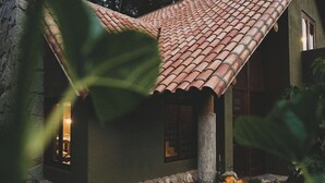 A house with a tiled roof, a stone pillar, and a window with a warm light inside.