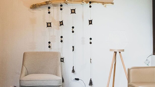A cozy living room with a wooden ceiling, a hanging decorative piece, a sofa, a coffee table with a plant, and a small lamp.