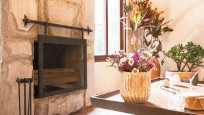 A stone wall with a fireplace, a wooden vase with flowers, and a window with a view of greenery.
