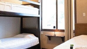 A room with bunk beds, a window with curtains, a shelf, and a small plant.