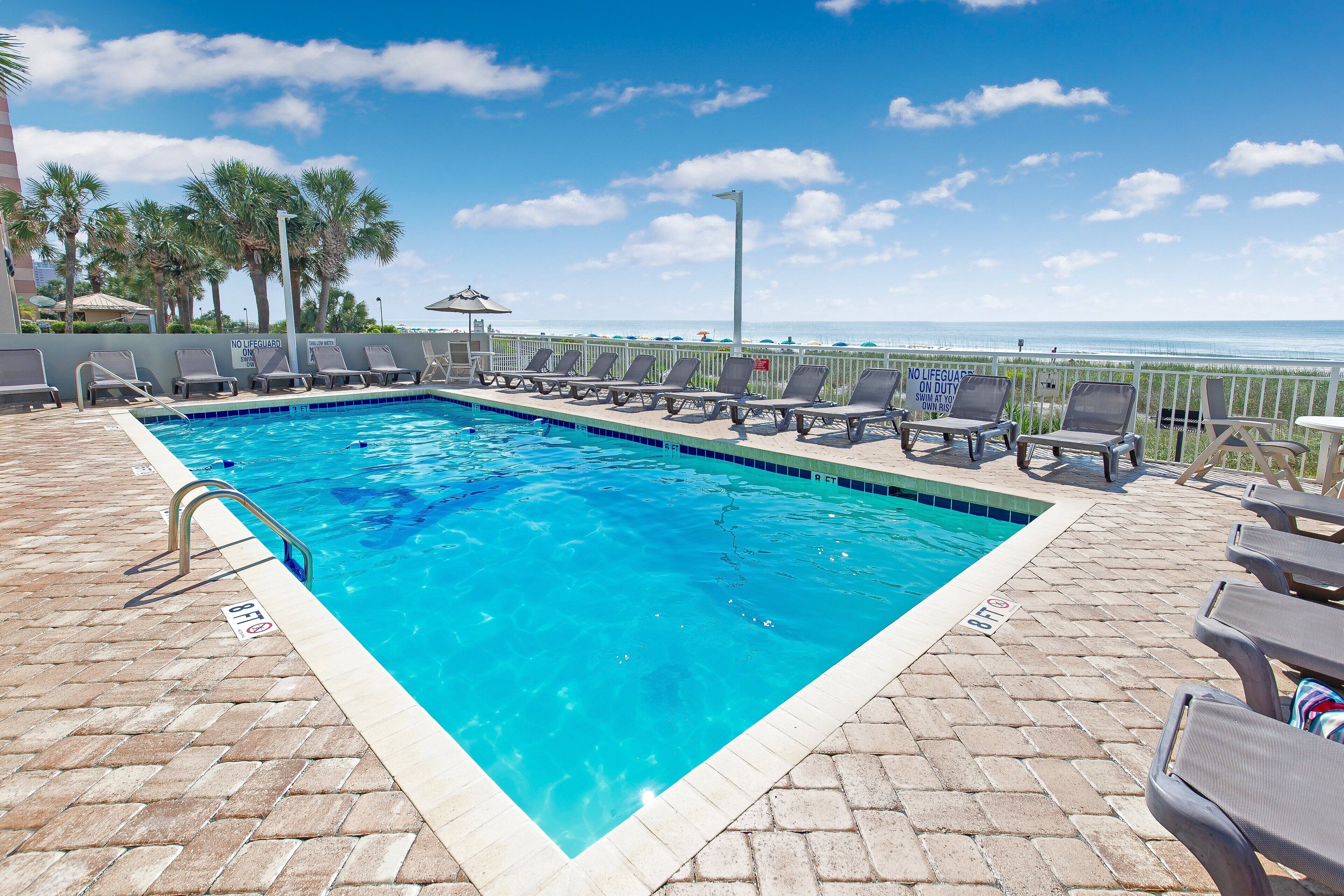 A swimming pool with lounge chairs and a view of the ocean.