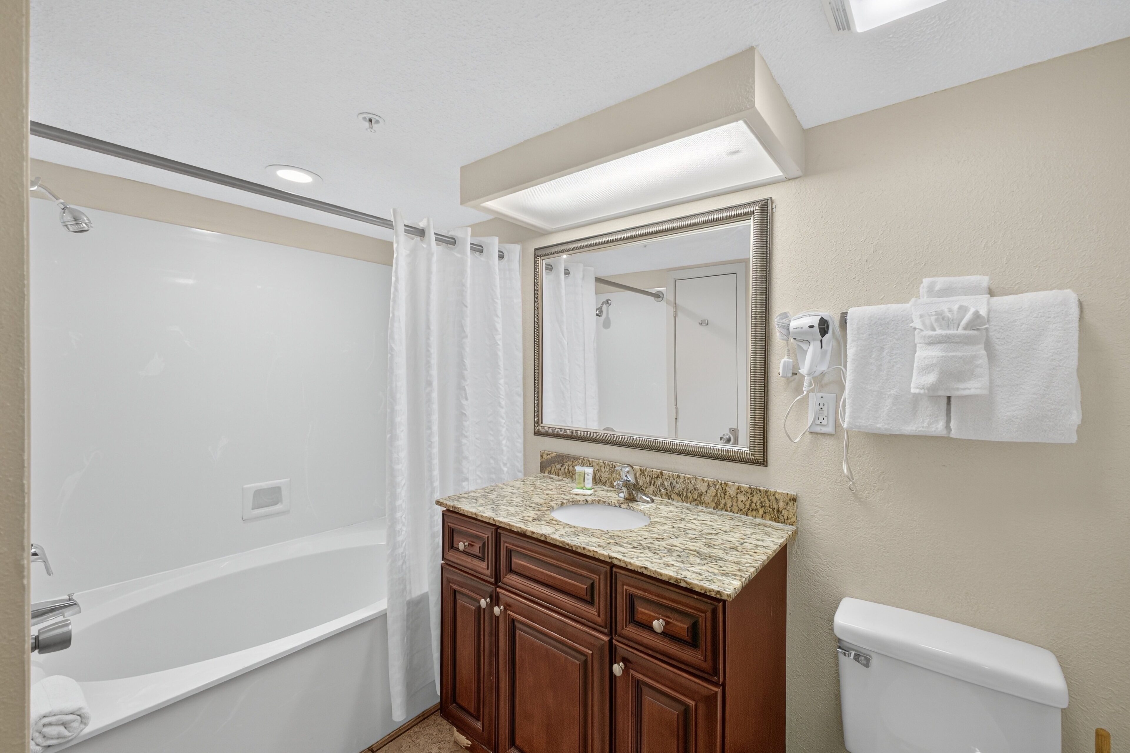 A modern bathroom with a bathtub, a sink, a vanity with drawers, a toilet, and a mirror.