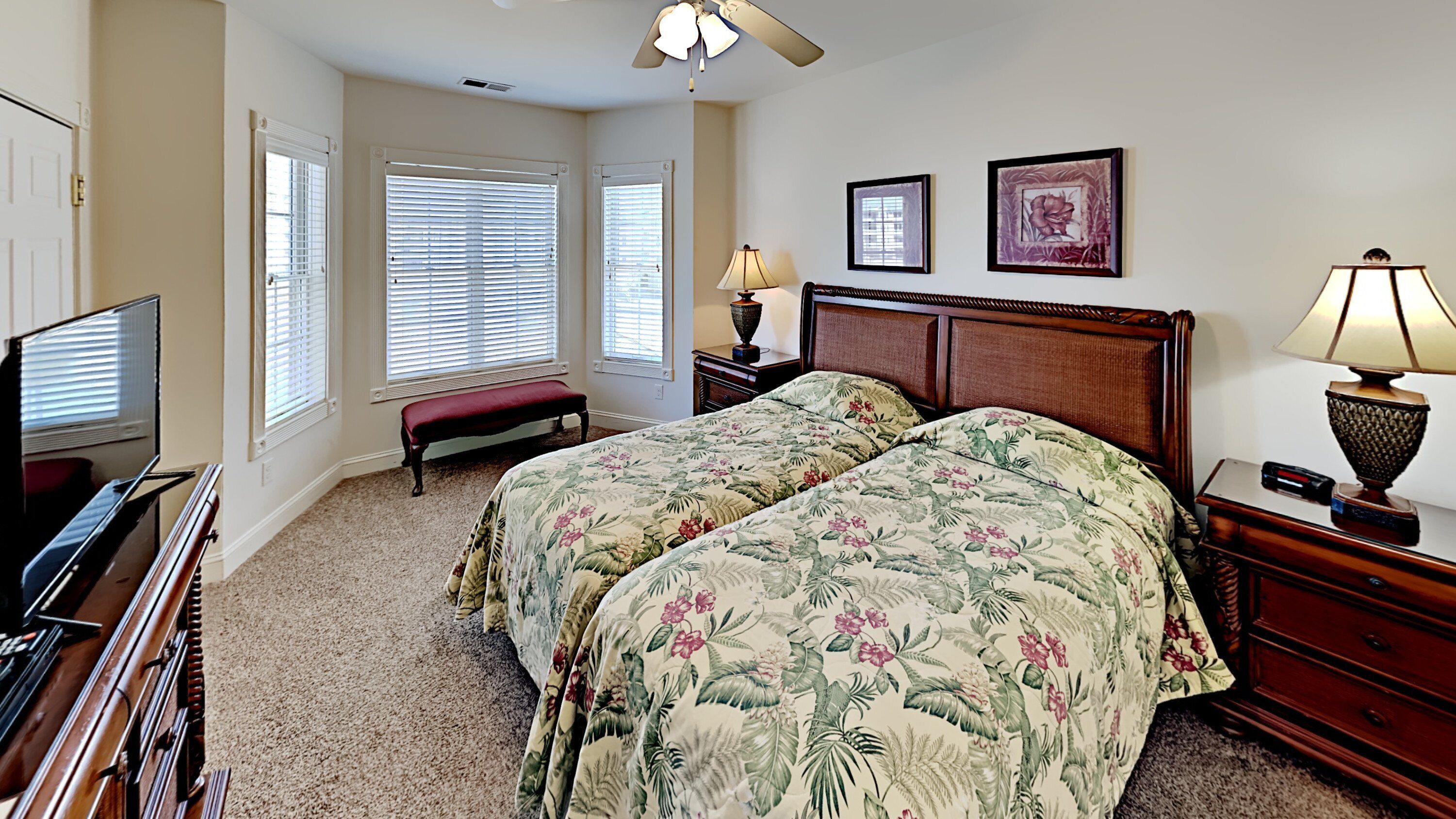 A bedroom with two beds, a TV, a bench, a desk, and a lamp.
