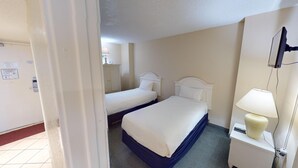 Una camera d'albergo con due letti singoli, un comodino con lampada, una TV montata a parete e una porta che dà su un'altra stanza.
