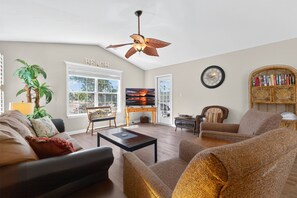A living room with a ceiling fan, a television, a bookshelf, and a large window. - Fairways 26E (Myrtle Beach)