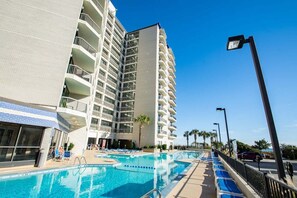 A hotel with a swimming pool, multiple balconies, and a clear blue sky. - Carolina Winds 806 (Myrtle Beach)