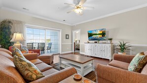 A spacious living room with a ceiling fan, a television, and a view of the outdoors through large windows. - Magnolia Pointe Magnolia Lake 4812-302 (Myrtle Beach)