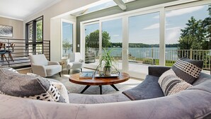 Un salon spacieux avec une grande fenêtre donnant sur un lac, une table basse ronde et des sièges confortables.