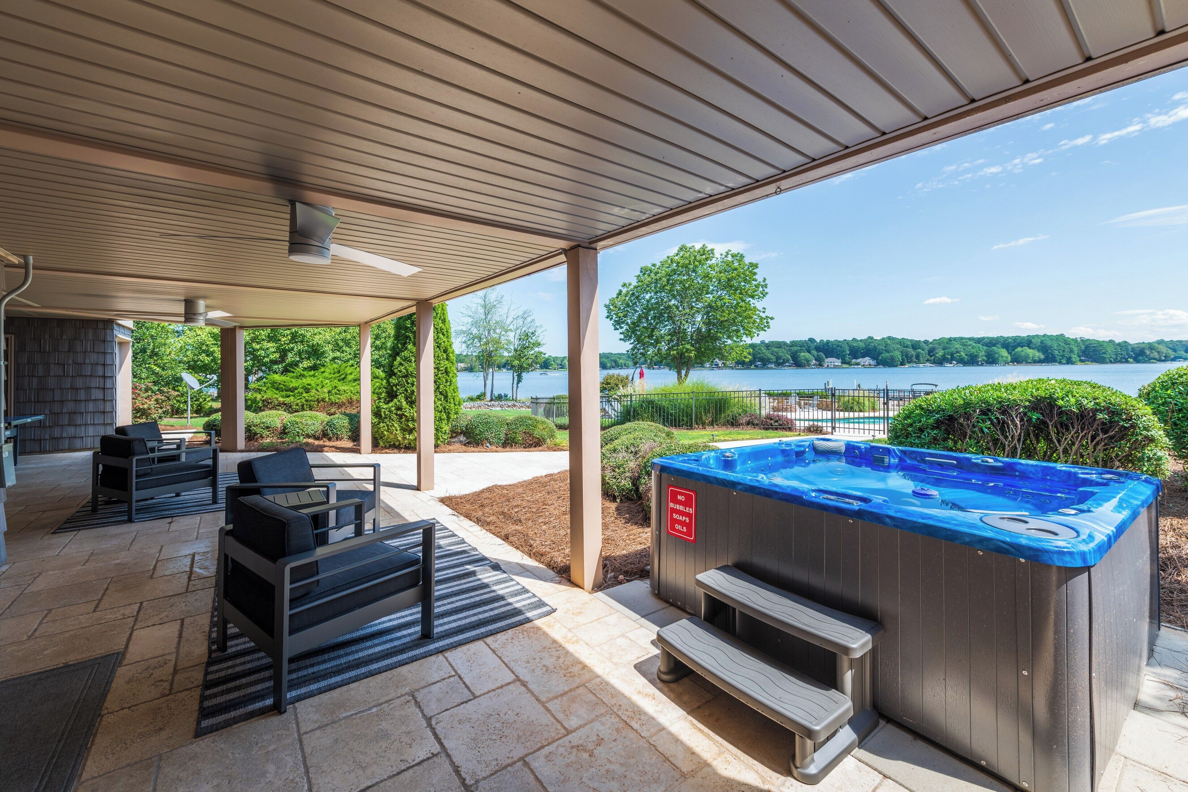 An outdoor patio with a hot tub, seating area, and a view of a lake.