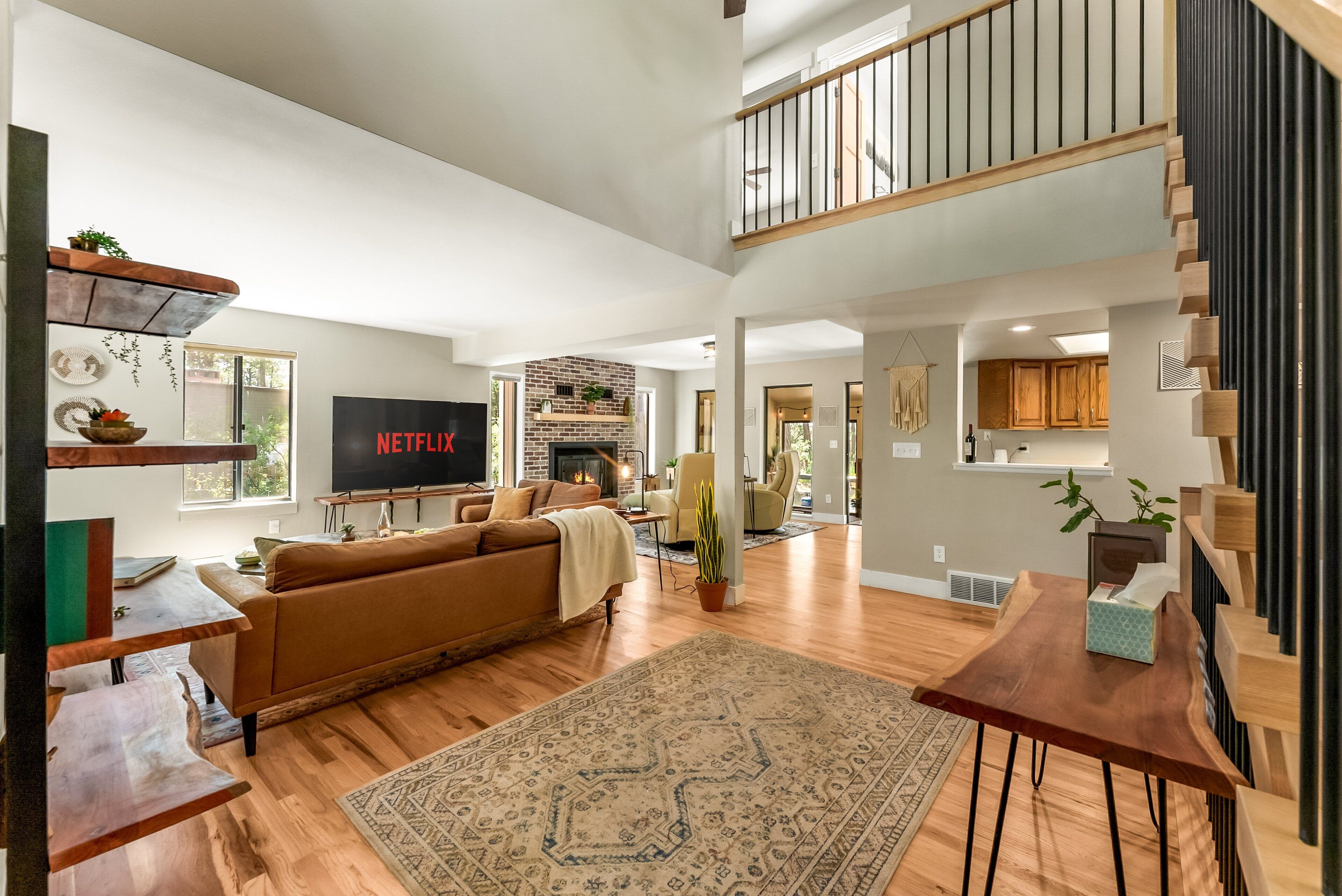 A spacious living room with a large TV, wooden flooring, a fireplace, and a staircase leading to an upper level.