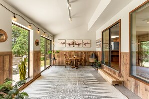 Un espace intérieur spacieux, doté d’une grande fenêtre, de murs en bois, d’un tapis à motifs et d’une table à manger avec des chaises.