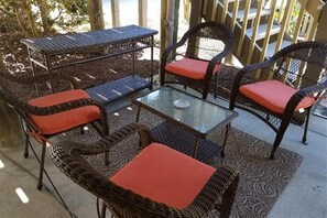 Un espace extérieur aménagé avec des meubles en osier, comprenant une table et des chaises en verre, une table en métal avec un banc, et un tapis à motifs.