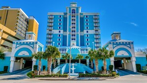 A large hotel with a central tower, multiple balconies, and a fountain in the entrance area. - Ocean Blue 303 (Myrtle Beach)
