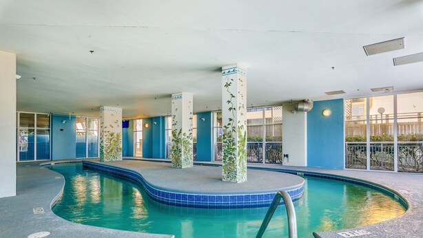 An indoor swimming pool with blue-tiled edges, a central island, and pillars with green vines. - Ocean Blue 303 (Myrtle Beach)