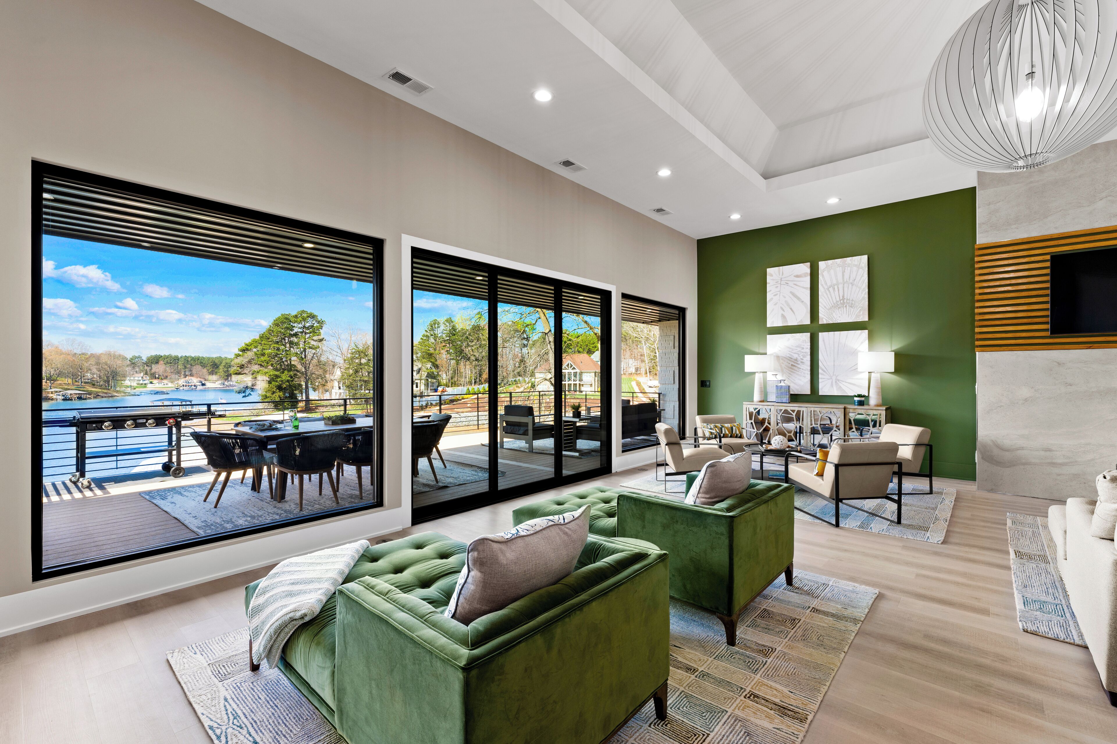 Un salón moderno con ventanas amplias, sofás verdes y vistas a un lago.