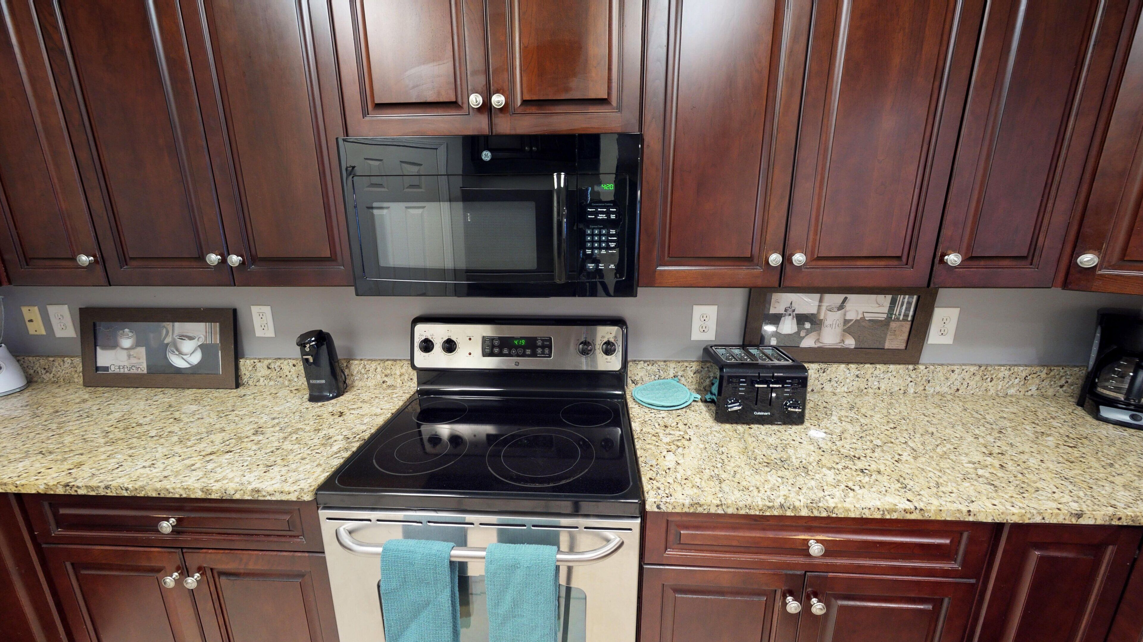 A kitchen with dark wooden cabinets, a black microwave, a stainless steel stove, and a toaster.