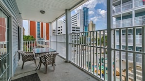 A balcony with a table and chairs, overlooking a street with buildings and a playground. - Myrtle Beach Villas 205 A (Myrtle Beach)