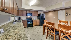 A kitchen with granite countertops, wooden cabinets, a microwave, stove, refrigerator, and a dining table with chairs. - Myrtle Beach Villas 205 A (Myrtle Beach)
