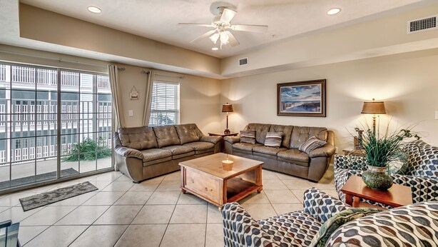 A spacious living room with a large window, a ceiling fan, and a view of the cityscape. - Myrtle Beach Villas 205 A (Myrtle Beach)
